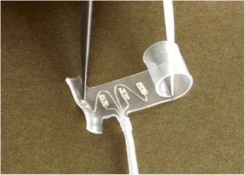 Photograph of a transparent self-curling spiral nerve cuff with four metallic stimulation contacts and a lead wire.
