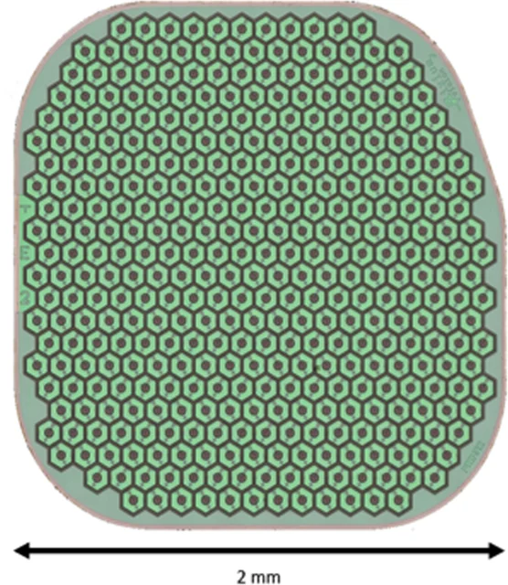 Optical micrograph of the PRIMA subretinal photovoltaic chip showing a dense hexagonal pixel lattice on a rounded square implant, with a 2 mm dimension marker.